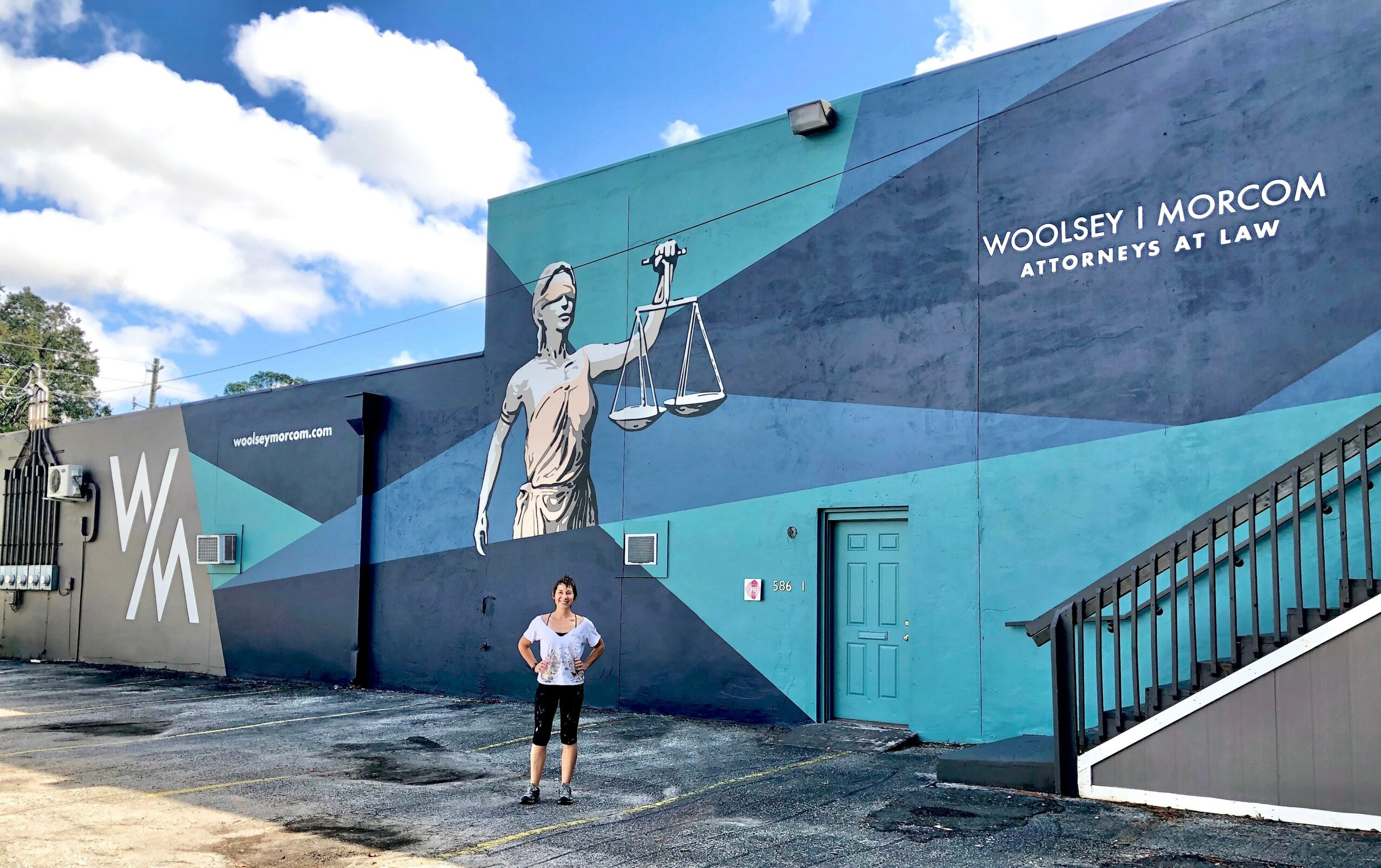 Person standing in front of a large mural of Lady Justice holding scales, with text about Woolsey Morcom attorneys at law.
