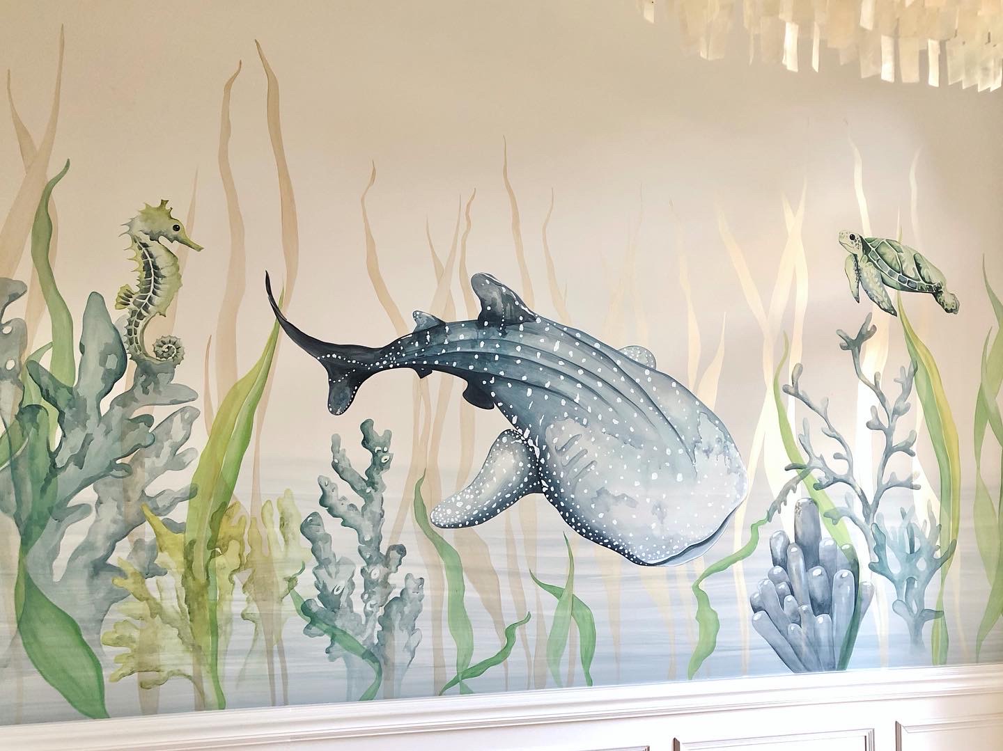 Underwater scene with a large whale, seahorse, and fish among seaweed and coral, painted in soft colors.